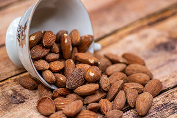Close up roasted organic brown almond seed on wooden table and some of almond in white porcelain cup