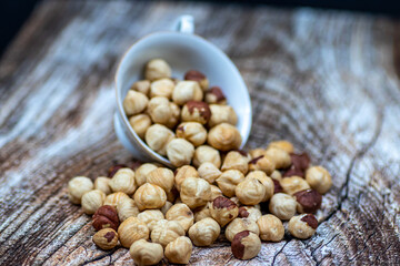 Peeled and roasted organically grown hazelnuts spilling out of a ceramic bowl on wooden table, close-up of healthy roasted hazelnuts, healthy snacks