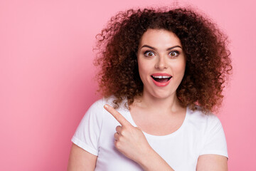 Portrait of impressed girl with wavy hairstyle wear white t-shirt indicating at sale empty space isolated on pink color background