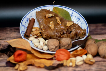 Turkish Baklava sweet cake on the plate, decorated with fresh pistachios, nuts, vanilla and dry autumn leaves, on wooden massive table  