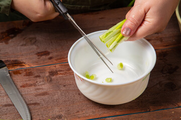 Green onions are cut with scissors into a white salad bowl