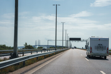 Traveling on a multilane highway, a white caravan is seen in the right lane under a partly cloudy...