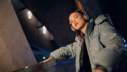 Fashion model posing headphones at night city close up. Woman eating lollipop.