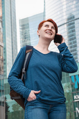 woman with red hair stands in a modern business district and talking on the phone