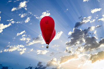 Red heart-shaped hot air balloon flying over a blue sky with white clouds	
