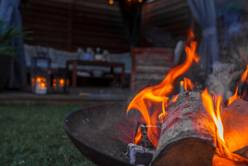 Evening ambiance with a lively fire in a metal pit, casting a warm glow in a garden with a wooden...