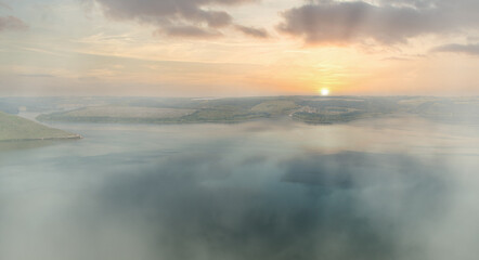Hazy sunrise over a calm lake with gentle hills in the background. Eco optimism concept.