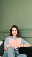 Happy young woman reading a book sitting comfortably on the couch enjoying a relaxing evening. Relaxed young woman enjoying a relaxing evening reading sitting on the couch. Rest and relaxation.