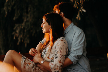 Happy, smiling couple in a green park with the sunset light, hugging, kissing, walking hand in...