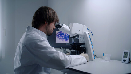 Male scientist looks under microscope, analyzes bacteria or blood sample in modern biotechnology...