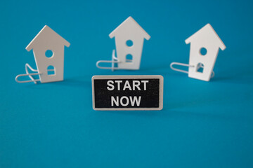 Start now symbol. Concept words Start now on black blackboard near miniature houses. Beautiful blue background. Business marketing, motivational start now concept.