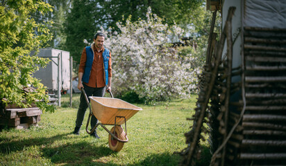 Portrait of a young farmer, a gardener with a garden cart on a plot of land in spring.