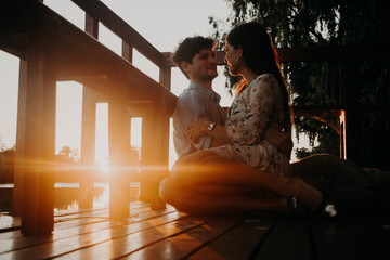 Happy, smiling couple in a green park with the sunset light, hugging, kissing, walking hand in hand, and lying on the ground, representing sincere love. Orange sun in the background