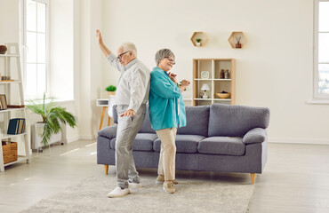 Happy senior family couple having fun at home. Cheerful funny old man and woman dancing together in...