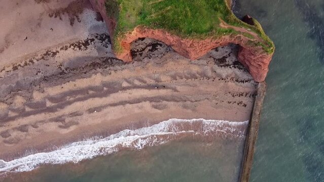 birds circleing above red langstone rock cliffs next to the beach an ocean drone footage, england, dawlish warren