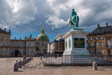 A historic European square features an oxidized bronze equestrian statue on a stone pedestal, surrounded by classical buildings with a baroque dome, likely in Copenhagen.