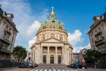 Copenhagen's Frederik's Church, The Marble Church, has a rococo style and a green copper dome with a gold orb and cross. Its grand front showcases Corinthian columns under a striking sky.