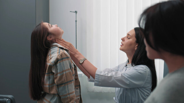 Female endocrinologist checks thyroid gland of Asian girl in hospital. Young patient undergoes examination or does checkup in clinic. Mother talks with medical professional. Concept of healthcare.