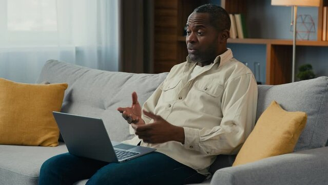 Annoyed dissatisfied stressed african american man male client customer businessman freelancer talking angry on video call using laptop at home on couch conflict quarrel arguing at online conference