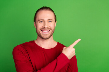 Portrait of toothy beaming guy with long hairstyle wear red sweatshirt indicating at offer empty space isolated on green color background