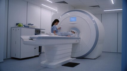 Female doctor, radiologist controls and turns on MRI or CT scan machine for female patient....