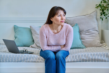 Middle aged woman experiencing abdominal pain sitting on couch at home