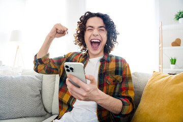 Photo of lucky funny guy wear plaid shirt rising fist winning game modern device indoors room home...