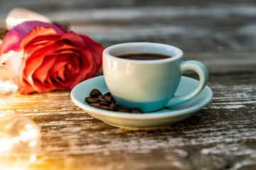 Blue ceramic mug on a vintage wooden background, coffee grains. Pink rose.