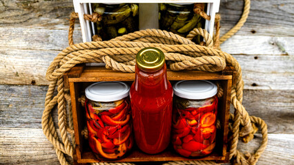 Wooden crate with bottles with tomatoes sauce and glass jars with pickled red bell peppers isolated...