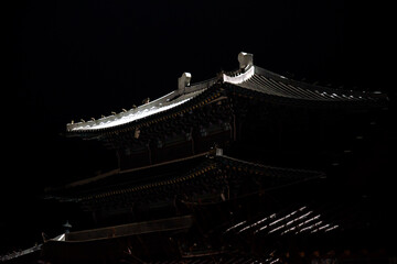 the snow-covered tiled roof of a traditional Korean building in the dark night