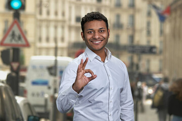 Successful Indian businessman showing okey symbol on blur city street. Success and achievement concept.
