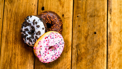 Colorful donuts on wooden table. Sweet icing sugar food with glazed sprinkles, doughnut with chocolate frosting. Top view with copy space