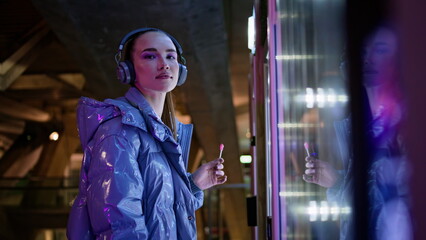 Girl touching snack automat making choice standing in night city subway close up