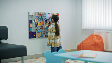 Little girl draws on entertainment board with toys in the waiting area in modern hospital. Child...