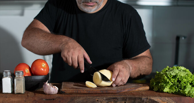 Hombre condimenta carne. Hombre prepara asado. Hombre latino prepara comida casera. Concepto de comida realizada en casa. Asado argentino.  Hombre corta papas. Hombre prepara una comida.