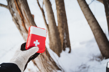 Holding a first aid kit in the winter forest. Cold weather survival kit.
