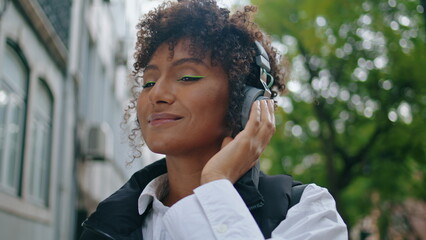 Girl listening music earphones standing city street closeup. Woman enjoying song