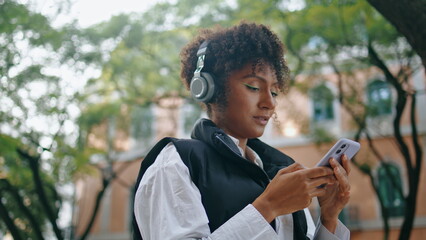 Girl earphones using phone app to listen music outdoor. Woman choosing song.