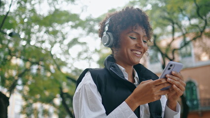 Cheerful lady listening music by wireless headphones holding phone close up.