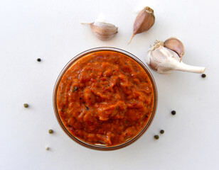 Bowl of red sauce, close-up,garlic on a white background. Homemade sauce, seasoning,spicy paste. Bulgarian lutenitsa, aur Balkan ajvar, with tomatoes, eggplants, paprika, garlic. Traditional seasoning