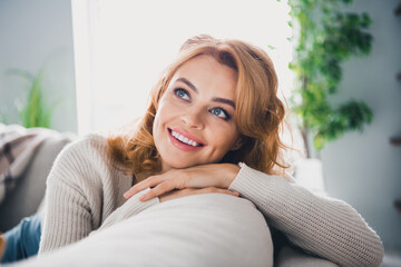 Portrait of peaceful pretty minded girl sit comfy sofa beaming smile look interested away inspiration free time apartment inside