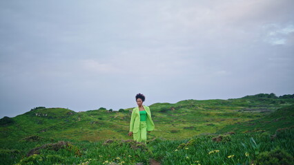 Stylish girl dancer performing modern style dance on green field under gray sky.