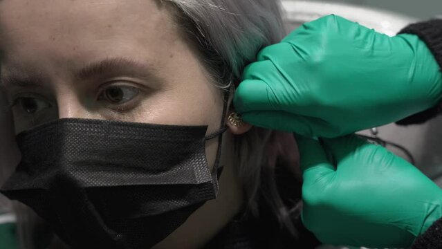 Caucasian woman having a piercing changed by a professional wearing green surgical gloves.