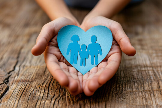 Hands holding a heart-shaped paper cutout with a family, symbolizing care and support for social issues like foster care and autism.