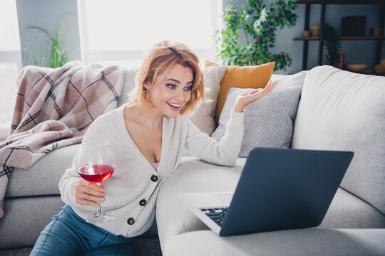 Portrait of pretty cheerful lady sit floor hold wine glass speak video call laptop sofa free time flat indoors - Powered by Adobe