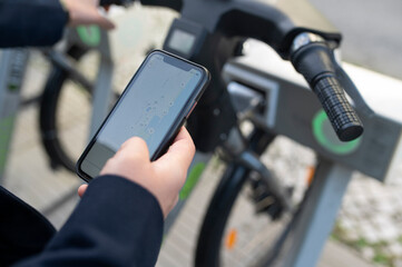 Hand of a man holding a phone with a scan code to unlock a rental city bicycle 