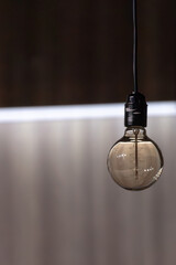 A round transparent electric light bulb on a dark background. Electric light source. Light symbol. Achievements of humanity. Evidence of progress. Hanging from the ceiling by a wire.