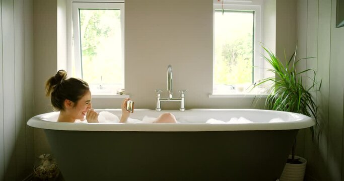 Bath, wellness or woman with smartphone, video call or relax on weekend break or conversation. Person, home or girl with cellphone or vacation with cleaning or online chat with mobile user or bubbles