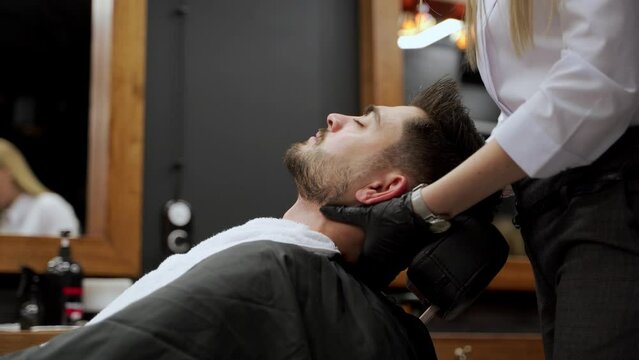 Relaxed man enjoys facial massage at barber shop. Professional beautician in gloves works on clients skin care. Gentle face therapy session enhances well-being at male spa salon.