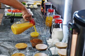A hand pouring orange juice from a pitcher into a glass on the buffet table during breakfast at the...